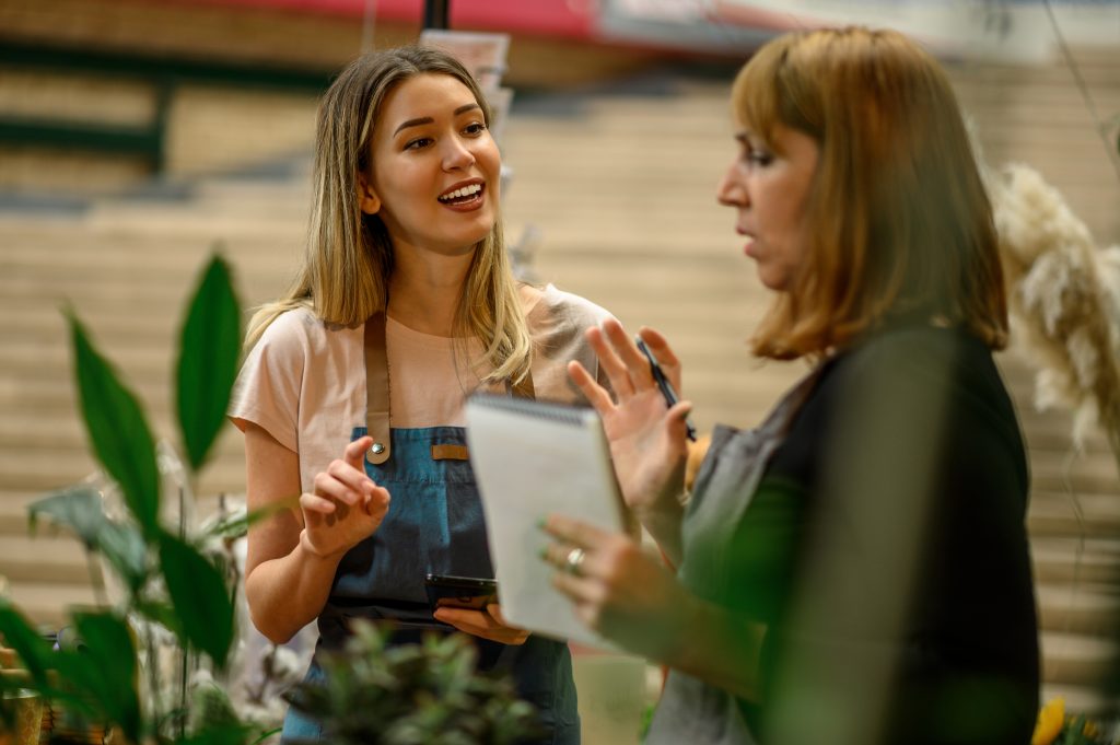 An experienced florist coaching a younger employee on looking after customers