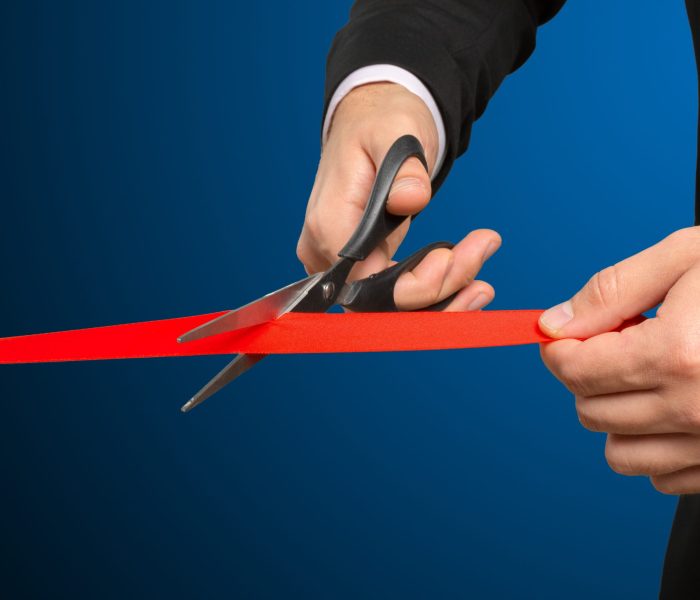 Businessman cutting red ribbon with pair of scissors