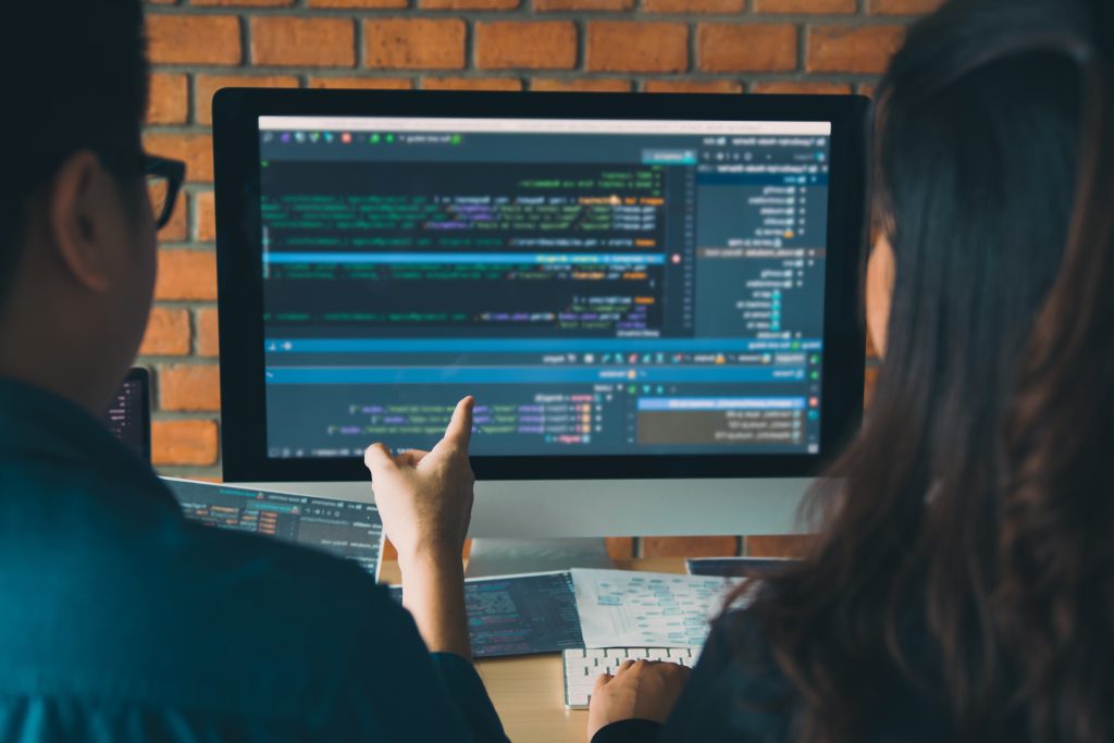 Two colleagues in a small business working through code together at a monitor