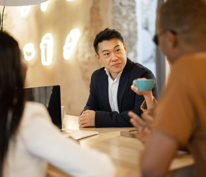 Multiracial business team watching something on laptop while working in cafe or restaurant. Concept of remote and freelance work. Idea of business cooperation. Smiling people sitting at wooden table
