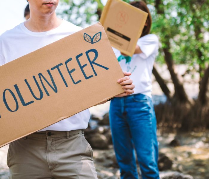 Close up volunteer man hold a volunteer sign in world environment day event, volunteer conservation pick up plastic and foam garbage on mangrove forest area.Volunteering save world concept.