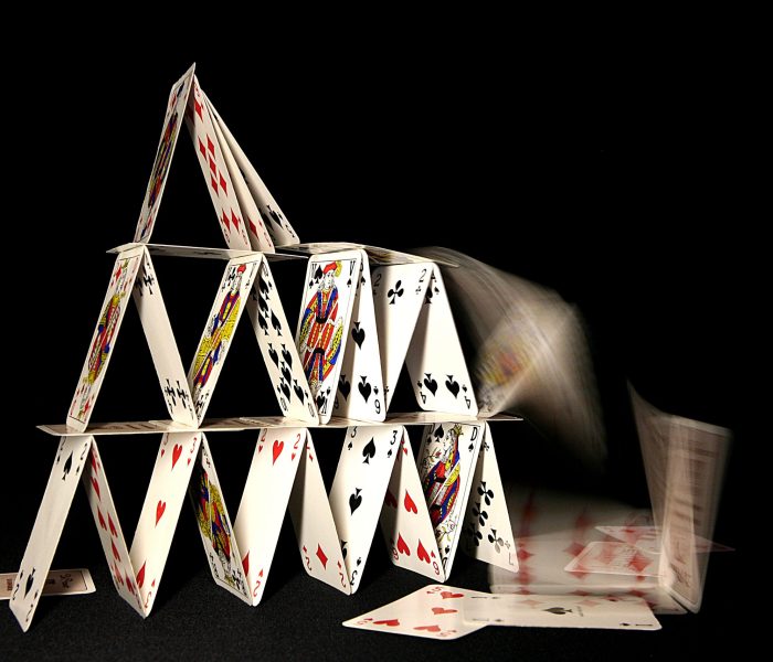 A house of cards collapsing on dark background