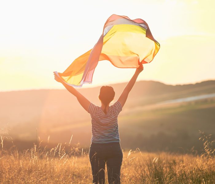 Young woman with LGBT flag. Woman holding a Gay Rainbow Flag in magic sunset. Happiness, freedom and love concept for same sex couples